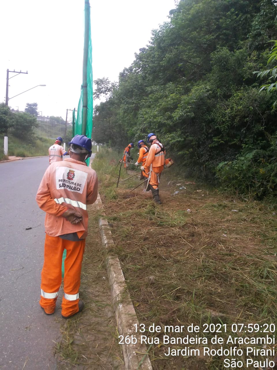 trabalhadores cortam grama numa calçada, com mata à direita. Foto identificada como rua Bandeira de Aracambi